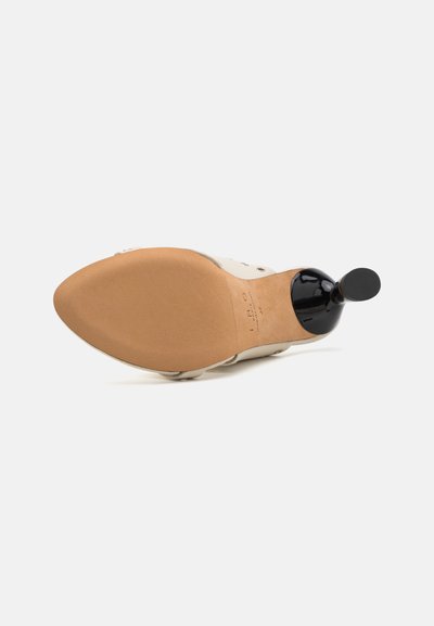 Beige schoen met een stevige tan zool en een ronde zwarte hak. De bovenzijde heeft een gladde textuur met minimale details en een klassiek ontwerp.