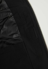 Nahaufnahme des Innenraums einer schwarzen Jacke mit glattem Futter, eingenähtem Fach und silbernem Reißverschluss entlang der Kante.