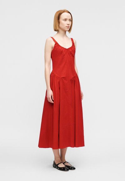 Κόκκινο βαμβακερό μίντι φόρεμα με λεπτές ράντες, σούρες στον λαιμό και φουσκωτή φούστα. Φορεμένο με μαύρα φλατ παπούτσια που έχουν κυκλικές λεπτομέρειες.