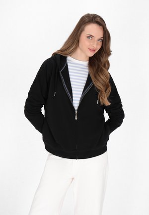 Black zip-up hoodie made of soft fabric, featuring a lined hood, front pockets, and silver zipper. Worn over a light striped shirt.