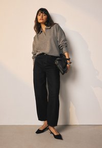 Grå sweater med krave, sorte højttaljede bukser og sorte slingback-sko, med en sort håndtaske med sølvfarvede hardware-detaljer.