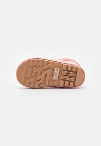 Sneaker rosa in gomma con suola testurizzata, caratterizzata da un battistrada decorato e branding. La suola ha un colore di contrasto marrone chiaro.