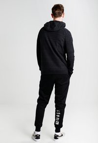 Svart hoodie med strukturerad tyg och dragskohuva, kombinerad med svarta joggers med vita grafiker. Skor i svart och vitt.