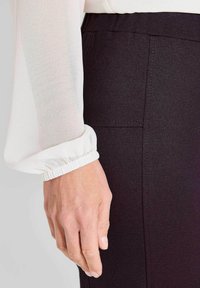 Witte blouse met lange mouwen en een geplooide manchette, gecombineerd met donkere, glad afgewerkte broek met zijzakken en minimalistische naden.