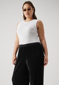 White ribbed tank top paired with black wide-leg corduroy pants featuring a black waistband, model wearing oversized sunglasses.