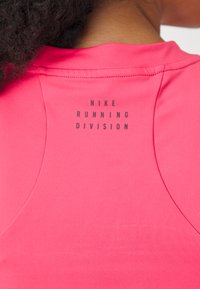 Růžová běžecká košile Nike s kulatým výstřihem a potiskem "NIKE RUNNING DIVISION" na zadní straně. Vyrobena z hladké, elastické tkaniny.