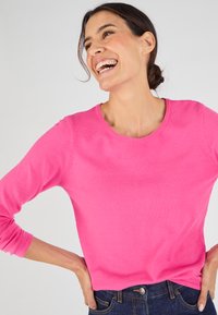 Roze gebreide trui met lange mouwen en ronde hals, met een gladde textuur en een aansluitende pasvorm, gecombineerd met blauwe denim jeans.