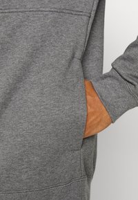 Šedá mikina s texturovaným povrchem, s klokaní kapsou a žebrovanými manžetami. Tkanina se zdá být měkká a mírně pružná.