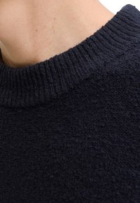 Maglione blu navy lavorato a maglia con superficie testurizzata e pelosa e scollo a girocollo a coste. Vista ravvicinata che mostra la morbidezza del tessuto.