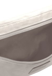 Pochette en toile avec une fermeture éclair, extérieur beige clair et doublure intérieure lisse. Présente une étiquette de marque discrète sur le côté.