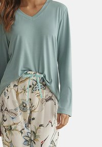 Haut à manches longues de couleur bleu-vert clair avec un décolleté en V et une coupe ample, associé à un pantalon crème à motifs comprenant des fleurs et des grues, noué à la taille.