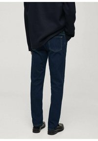 Tamno plave traperice s ravnim krojem, dizajnom s pet džepova i kontrastnim šavovima. Nosive s crnom majicom i crnim cipelama.