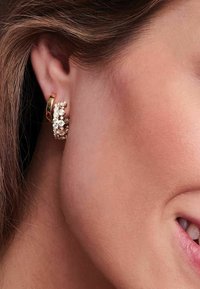 Guldtonade hoops med klara gemstonesmyckningar, med en strukturerad design och texturerad yta för extra detalj.