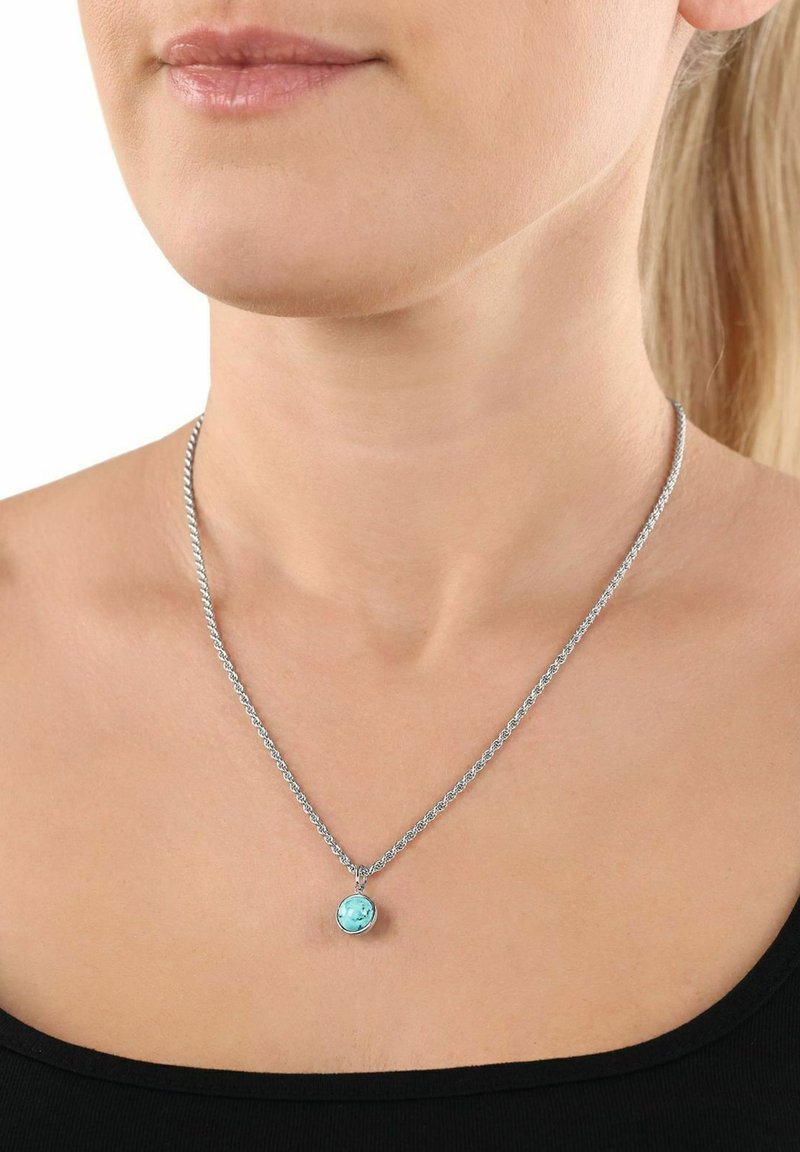 Silverfärgad kedja med ett runt ljusblått hänge. Hänget har en slät yta och är inneslutet i en liten metallram.