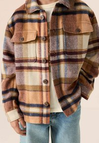 Geruit flanellen overhemd in oranje, bruin, crème en blauwe tinten, met twee borstzakken, bruine knopen en een comfortabele pasvorm.