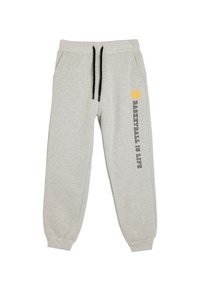 Pantalones de chándal gris claro con cordones negros, bolsillos laterales, puños acanalados y el texto "El baloncesto es la vida" junto a un ícono de baloncesto amarillo en una pierna.