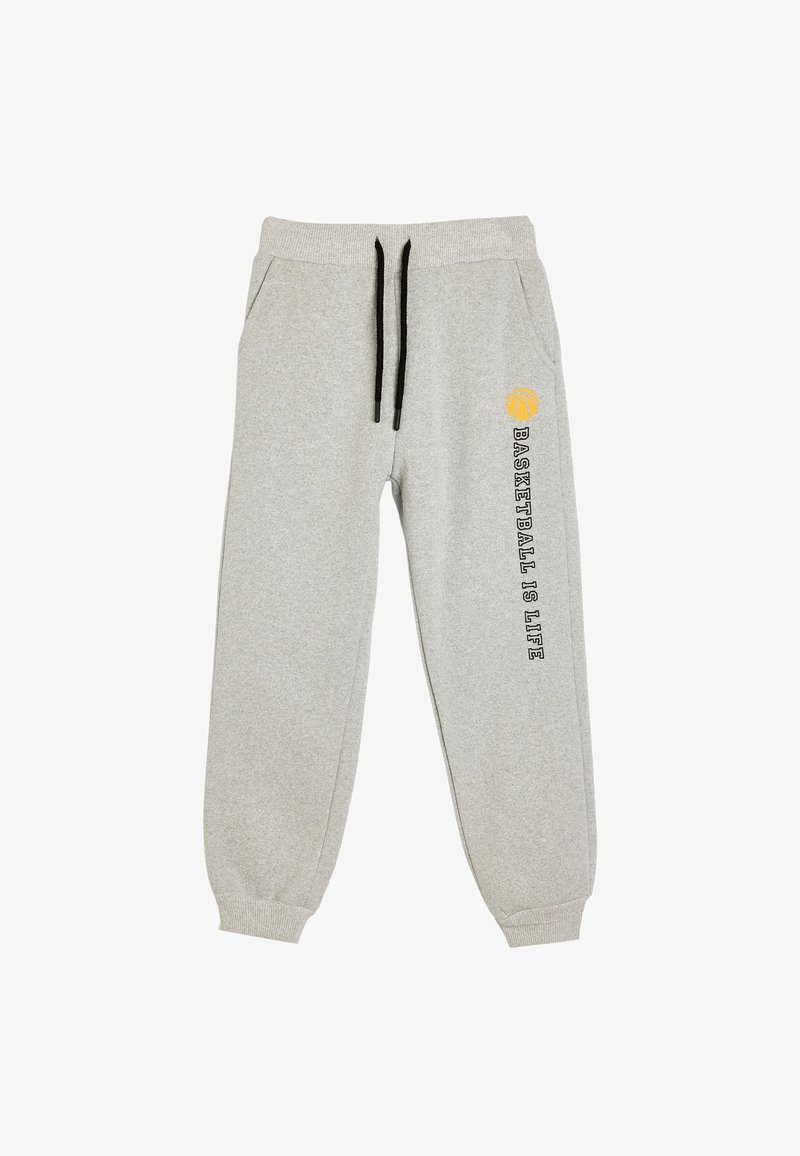 Pantalones de chándal gris claro con cordones negros, bolsillos laterales, puños acanalados y el texto "El baloncesto es la vida" junto a un ícono de baloncesto amarillo en una pierna.