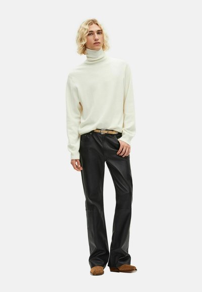 Jersey de cuello alto crema combinado con pantalones de cuero negros y zapatos color marrón claro, con una cintura ceñida y una tela suave y texturizada.