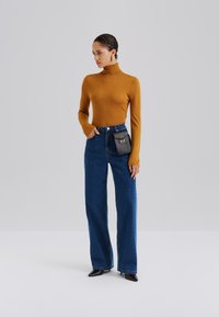 Mustár sárga garbó pulóver, magas derekú sötétkék széles szárú farmer, fekete táska fémes díszítéssel, és hegyes orrú magas sarkú cipő.