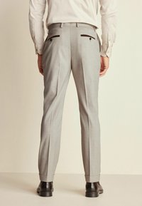 Pantaloni gri croiți cu pliu presat, două buzunare la spate cu accente închise, terminați cu mansete înguste, asortați cu pantofi negri.