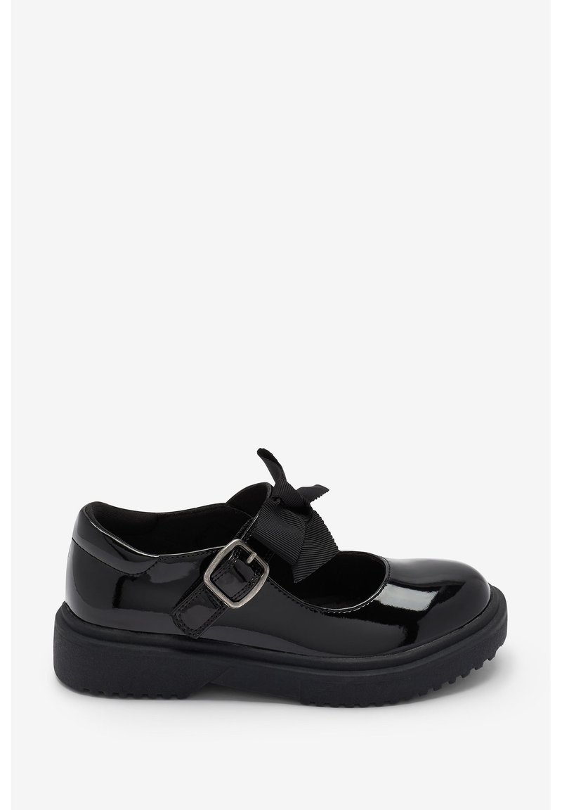 Chaussure Mary Jane en cuir verni noir avec un bout rond, fermeture à boucle et un accent en nœud sur la sangle. Semelle en caoutchouc épaisse avec traction.