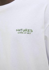 Hvid bomulds t-shirt med grøn tekst, der står "NATURE'S WORK OF ART." Glat tekstur med klassisk rund halsudskæring.