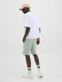 Wit oversized t-shirt, lichtgroene shorts, roze pet. Witte sneakers met textuurzolen. Gestreepte witte sokken. Schoon, minimalistisch ontwerp.