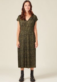 Vestido de estampado de leopardo en verde oscuro y negro, con escote en V, mangas cortas, falda plisada, y combinado con botas de tobillo.