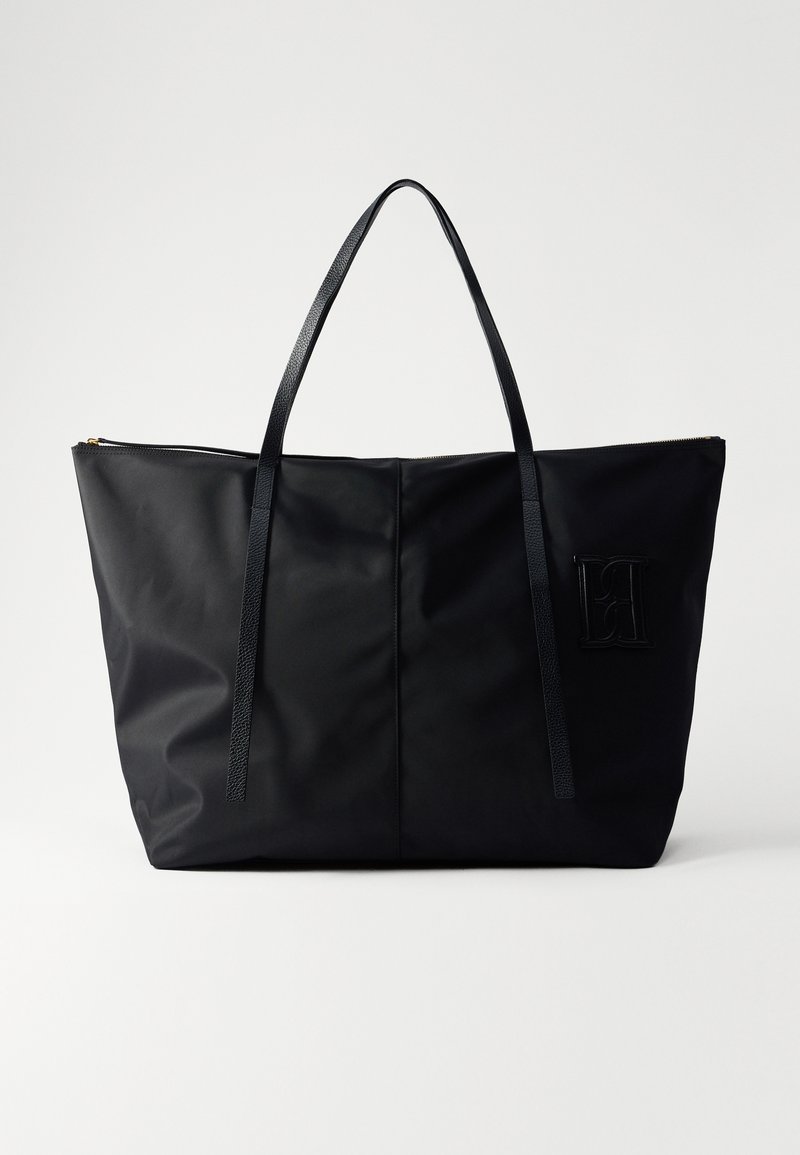 Fekete nylon bevásárlótáska texturált fogantyúkkal, nagy nyitott tetejével, diszkrét logóval és letisztult, minimalista kialakítással.