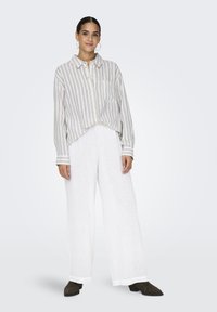 Chemise à rayures en tissu léger, associée à un pantalon large en lin blanc. Chaussures brunes, coupe décontractée et détail de poche poitrine.
