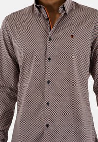 Chemise à manches longues, boutonnée, en tissu à motifs. Présente un motif géométrique en marine, orange et blanc, avec des boutons noirs et un accent orange à l'intérieur du col.