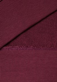 Tejido burdeos con textura acanalada, que presenta una superficie suave y lisa con detalles de borde en contraste. Adecuado para uso en ropa.