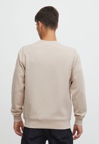 Beige sweatshirt with a crew neck and ribbed cuffs, made from soft, smooth fabric. Features a plain design, no visible patterns or logos.