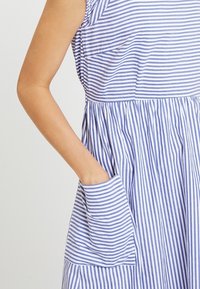 Sininen ja valkoinen raidallinen mekko, jossa on levenevä muotoilu, hihaton malli ja sivutasku, jossa on taitettu reuna.