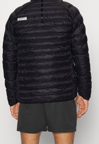 Černá péřová bunda s horizontálním prošíváním, lesklou texturou a logem Puma na horní části zad. Obsahuje vysoký límec a štíhlý střih.