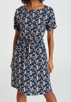 Frau trägt ein knielanges blaues Kleid mit kurzen Ärmeln, tailliert und mit mehrfarbigem abstraktem Blumenmuster.