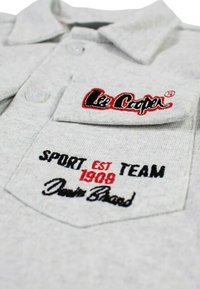 Gros plan d'une chemise grise avec une poche boutonnée affichant le logo brodé Lee Cooper et le texte : "SPORT TEAM EST 1908 Denim Brand."