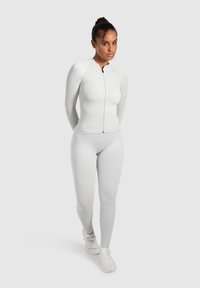 Hvid fitted sportsoberdel med lynlås og lange ærmer, parret med matchende slim-fit leggings, begge lavet af struktureret stof.