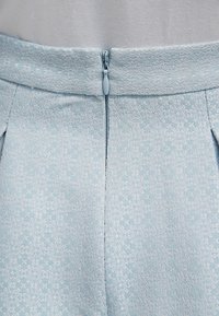 Tessuto azzurro chiaro con motivo floreale sottile, caratterizzato da una cerniera posteriore e pieghe in vita. Finitura liscia.