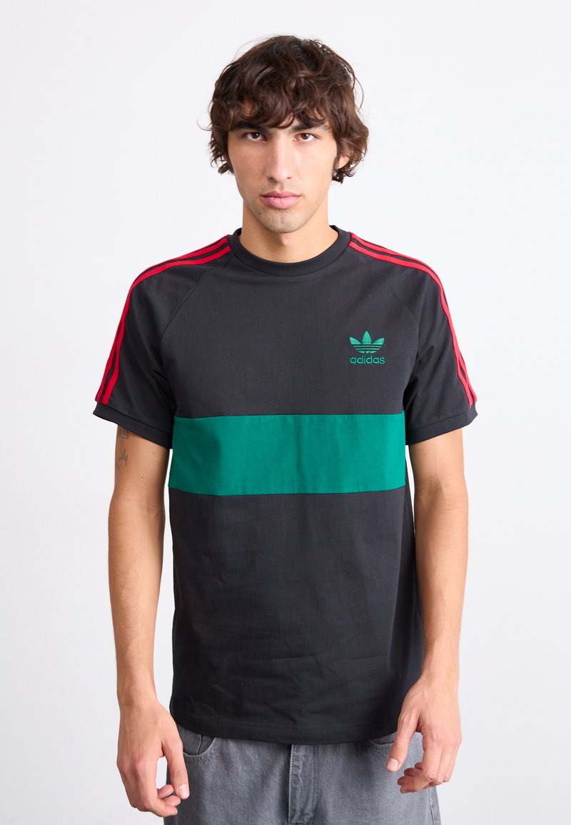 Juodas medvilninis marškinėliai su žalia horizontalia juostele ir raudonomis petnešomis; žalia Adidas logotipas krūtinėje; trumpomis rankovėmis.