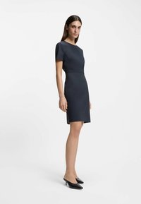 Navy blue short-sleeve dress with a fitted bodice and flared skirt, made of textured fabric. Worn with black high-heeled shoes.