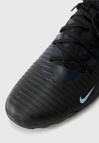 Black Nike soccer shoe with textured synthetic upper, featuring horizontal ridges and a blue logo. Laces are black, and the sole is rubber.