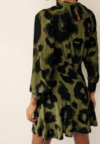 Robe verte avec imprimé léopard noir, tissu texturé, manches bouffantes, dos en trou de serrure et jupe évasée.