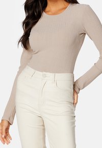 Langsleeve ribbeltop van beige stof, gecombineerd met hooggetailleerde crèmekleurige broek met zijzakken en een knoopsluiting.