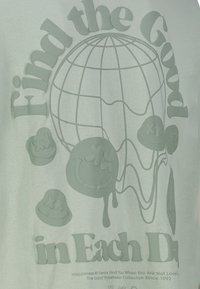 Mint green t-shirt with raised textual and graphic design featuring a globe and smiley faces. Soft fabric with smooth texture.