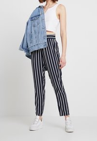 Randiga byxor i marinblått och vitt med elastisk midja, kombinerade med en kortärmad vit, ribbad linne och en jeansjacka över axeln.