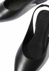 Scarpe slingback in pelle nera con punta affusolata e design minimalista, dotate di tacco basso e superficie liscia.