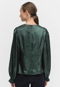 Zielona satynowa bluzka z okrągłym dekoltem, długimi bufkami z elastycznymi mankietami oraz zapięciem na zamek z tyłu. Gładka tekstura.