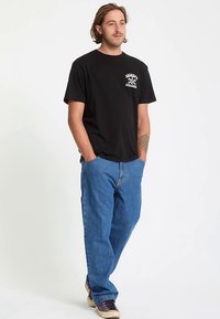 Schwarzes Baumwoll-T-Shirt mit kurzen Ärmeln und einem Grafikdruck auf der Vorderseite, kombiniert mit blauen Denim-Cargohosen mit Taschen und entspannter Passform.