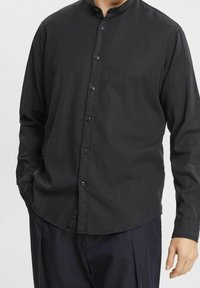 Camicia nera con colletto alla coreana, realizzata in un tessuto morbido. Presenta una patta frontale e maniche lunghe con polsini abbottonati.